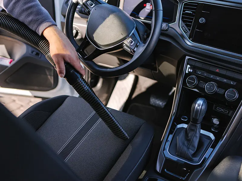 Un homme utilise un aspirateur pour nettoyer l'intérieur de sa voiture.
