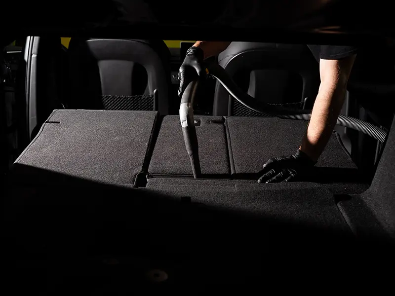 Un homme utilise un aspirateur pour nettoyer l'intérieur de sa voiture.